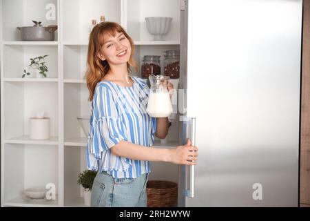 Young woman with jug of milk near fridge in kitchen Stock Photo