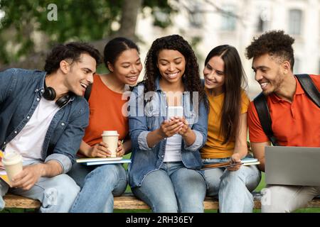 Nice App. Group Of Multiethnic Students Using Smartphone Together Outdoors Stock Photo