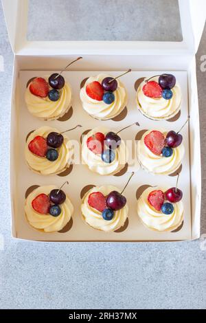 Close up on a set of cupcakes decorated with strawberry slices, fresh raspberry and blueberry on gift box Stock Photo