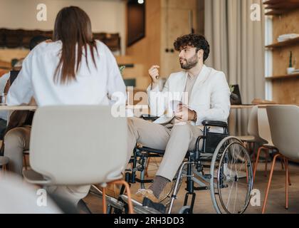In the corner of the coffee shop two students collaborate on a project, while a freelancer works on a proposal at a nearby table Stock Photo