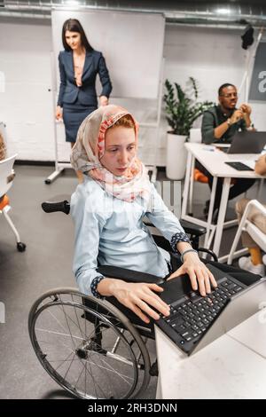 Handicapped businesswoman in wheelchair at meeting. Paralyzed woman in a wheelchair working on lap top Stock Photo