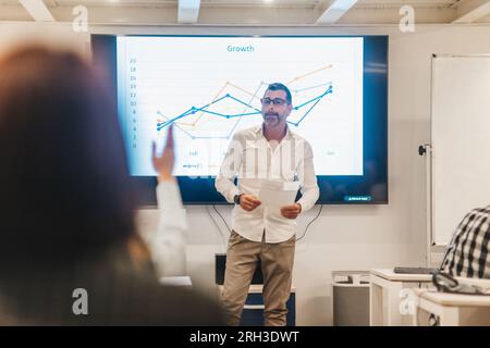 Good looking 50s business coach answering employees questions after presentation at the classroom Stock Photo