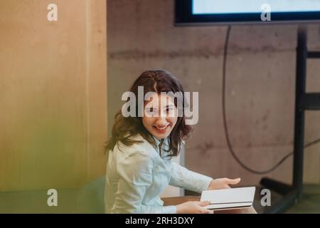 Beautiful brunette female employee smiling while having fun conversation with colleague during break at work Stock Photo
