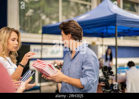 Lovely female student taking a red notebook for her friend from her male colleague at school Stock Photo