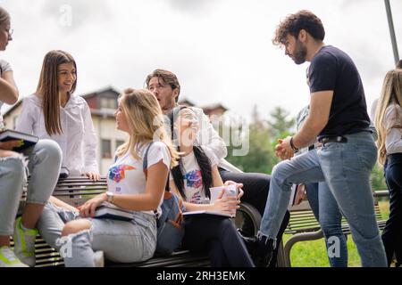 Young, happy, college students having a conversation sitting on a bench in the park out of the campus building, discussing school subjects or project, Stock Photo