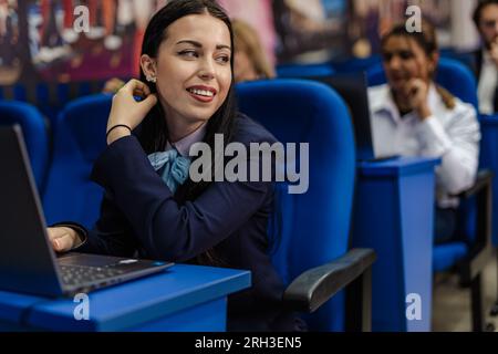 Female student working on her laptop with the other students while in class Stock Photo