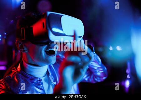 Neon metaverse futuristic concept. excited elegant 40 years old woman in vr headset testing out virtual reality. Stock Photo
