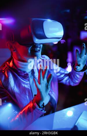 Neon metaverse futuristic concept. smiling stylish middle aged woman in vr headset designing metaverse. Stock Photo