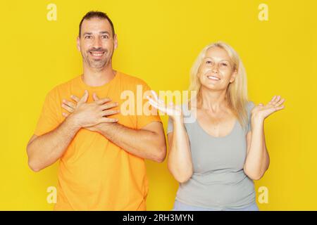 Caucasian couple in their 40s receiving amazing news that shocks them, isolated on yellow studio background. Stock Photo