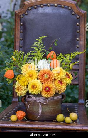 bouquet of yellow and orange dahlias, physalis and goldenrod in rustic pot on the old chair Stock Photo