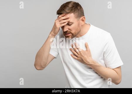 Unhealthy middle aged man presses hand to chest and head having heart pain, headache, dizziness Stock Photo