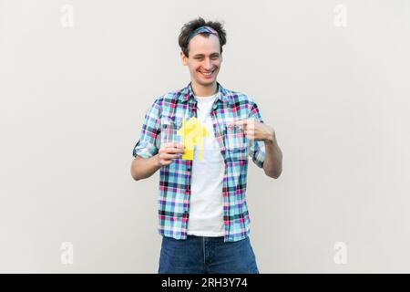 Portrait of nice attractive glad cheerful man holding in hands paper house form, sale bank loan purchase, wearing blue checkered shirt and headband. Indoor studio shot isolated on gray background. Stock Photo