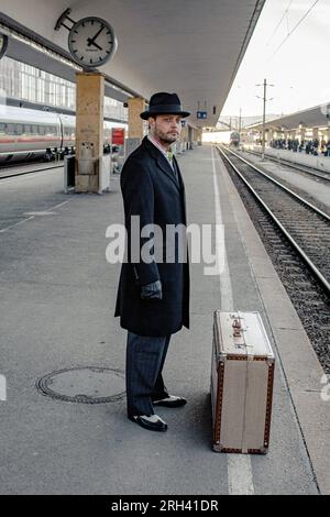 Male traveler waiting for travel on railway platform. Male standing with luggages at central station, train on time or delayed. Stock Photo