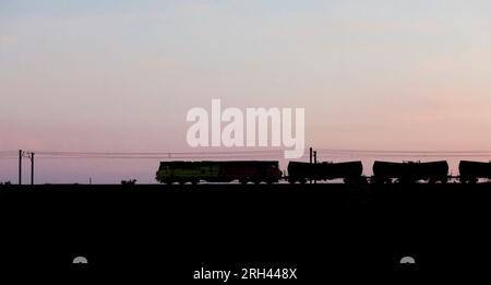 Colas Railfreight class 70 locomotive making a sunset silhouette at Kilwinning with a freight train carrying calcium carbonate Stock Photo
