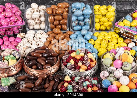 Heap of sugared almonds and hazelnuts dragees in chocolate isolated on dark background. Handmade colorful chocolate candies filled with nuts. Chocolat Stock Photo