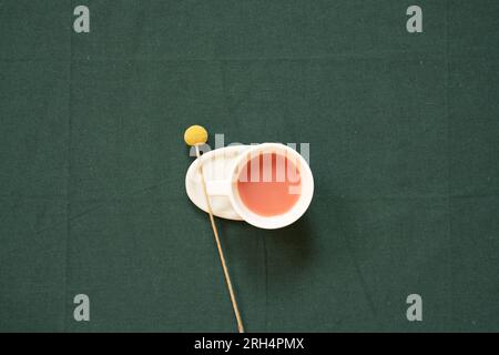 Cup of pink tea and yellow flower on green fabric table background. top view, copy space Stock Photo