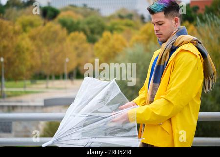 Man wearing a yellow raincoat closing an umbrella in autumn. Stock Photo