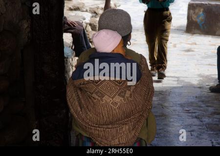 Lo Manthang, Nepal - July 23, 2023 : A rural mother carrying her child on her back in Nepal Stock Photo