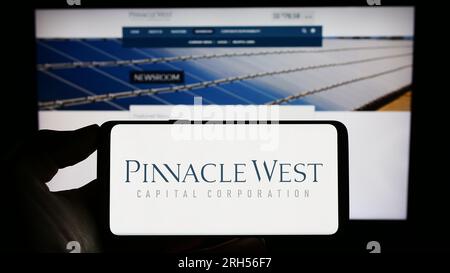 Person holding cellphone with logo of American company Pinnacle West Capital Corporation on screen in front of webpage. Focus on phone display. Stock Photo