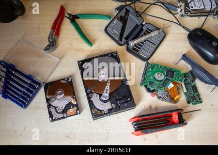 Electronic technician's work bench with a jumble of hand tools and computer components including two opened up hard discs. Stock Photo