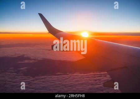 Airplane flight in sunset sky over ocean water and wing of plane. View from the window of the Aircraft. Traveling in air. Stock Photo