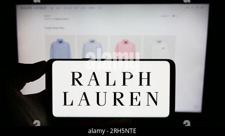 Person holding cellphone with logo of US fashion company Ralph Lauren Corporation on screen in front of business webpage. Focus on phone display. Stock Photo