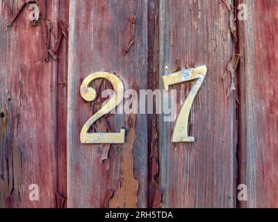 Number 27 on red painted old wooden wall. Red background. Stock Photo