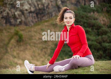 A young woman wearing leggings stretching in a public park in Edinburgh Stock Photo