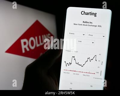 Person holding cellphone with website of US pest control company Rollins Inc. on screen in front of logo. Focus on center of phone display. Stock Photo
