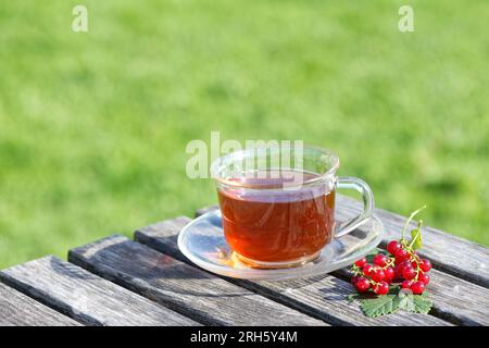 Glass cup of tea on a wooden rustic table and green grass on the background Stock Photo