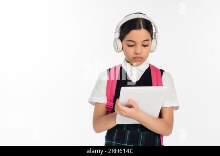 focused schoolgirl in wireless headphones using digital tablet isolated on white, digital age Stock Photo
