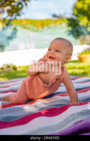 little baby smiling playing sitting on a colorful blanket in the garden at home. Stock Photo