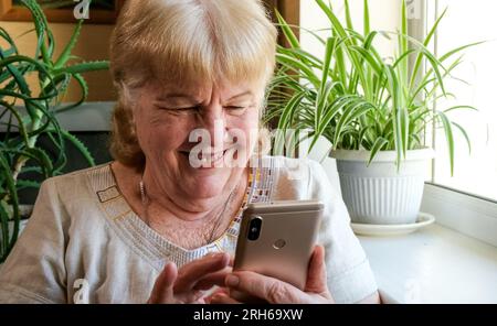 Happy smiling elderly woman using her phone at home. Grandma is typing text message Stock Photo