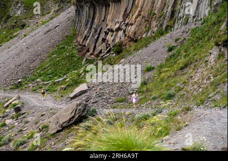 Mountain trekking. Man trekking high up in mountains. Hiker with trekking poles on slope against background of high snow-capped mountains Stock Photo