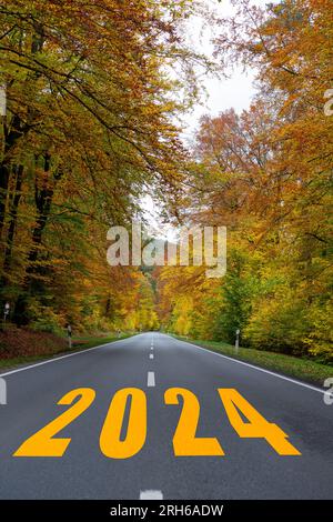 Start into the new year 2024. 2024 written on  road in the middle of empty asphalt road and beautiful autumn. Stock Photo