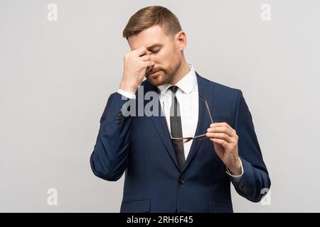 Tired exhausted man, businessman in suit, office worker takes off glasses on grey background. Stock Photo