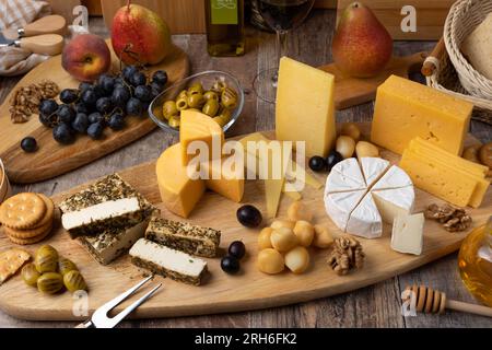 Cheese assorted on a wooden board, rustic style. Several sliced cheeses with pears, peaches, grapes, olives, honey, bread, crackers, walnuts and red w Stock Photo