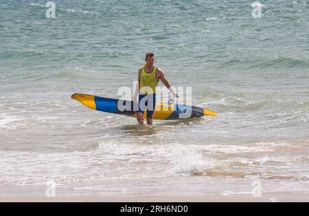 Man carrying surfski surf ski ready up the beach at Branksome Chine beach, Poole, Dorset, UK in August Stock Photo