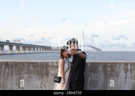 Shanghai, China. 25th July, 2023. Visitors take selfies with the Shanghai Yangtze River Bridge as background in Shanghai, east China, July 25, 2023. Chongming District and Pudong District of Shanghai, along with Qidong City of Jiangsu, are located in the estuary of Yangtze River. With its unique advantages, the region has been making concerted effort to further promote high-quality development. Credit: Jin Liwang/Xinhua/Alamy Live News Stock Photo