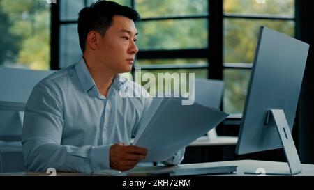 Professional asian businessman korean japanese 40s man lawyer office worker reading financial documents invoice contract budget documentation Stock Photo