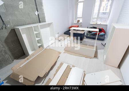 Parts of unfinished furniture, metal screws and tools lying on the floor with instruction manual for furniture assembly in the background. Moving to Stock Photo