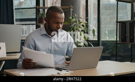 Tired exhausted African middle-aged office manager bookkeeper businessman American mature ethnic man read loan papers documents search mistake use Stock Photo