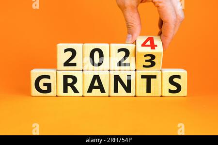 Planning 2024 grants new year symbol. Businessman turns a wooden cube and changes words Grants 2023 to Grants 2024. Beautiful orange background, copy Stock Photo