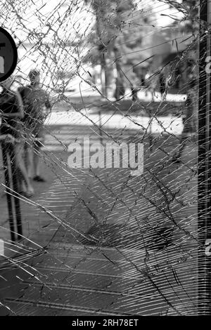 Broken glass of the front door of the supermarket. Modern fashionable glass armored door in a web of cracks after an act of vandalism during the war. Stock Photo