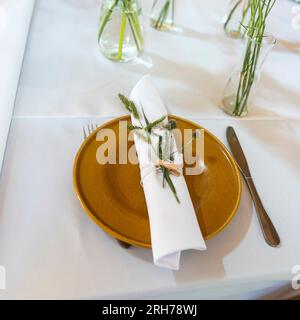Linen napkin folded into a tube, pinned with a clothespin and decorated with Eryngos and ears of rye on a blue plate on a served table Stock Photo