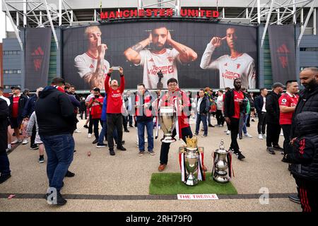 Manchester United fans pose for photographs with replica trophies outside the stadium ahead of the Premier League match at Old Trafford, Manchester. Picture date: Monday August 14, 2023. Stock Photo