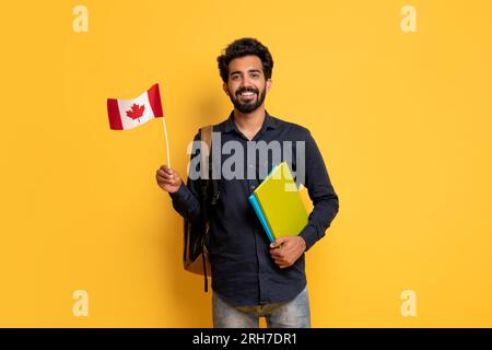 Smiling Indian Man With Canadian Flag And Workbooks Posing On Yellow Background Stock Photo