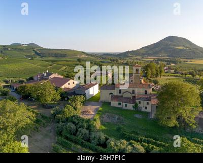 Old church in small rural village in the countryside in Italy in front of vast Italian green vineyard rolling hills landscape in summer Stock Photo