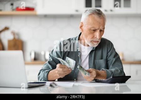 Senior Gentleman Planning Budget, Counting Money And Using Calculator In Kitchen Stock Photo
