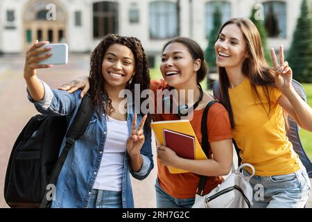 Three multiethnic female students talking selfie on smartphone outdoors Stock Photo